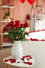 Vase with roses and engagement ring on table in bathroom decorated for Valentine's Day