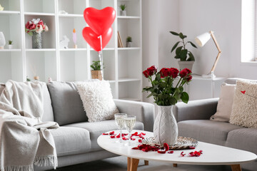 Vase with roses, engagement ring and champagne on table in living room decorated for Valentine's Day