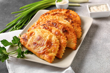 Plate with tasty chebureks, parsley, onion and sauce on grunge background