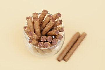 Glass of tasty wafer rolls with boiled condensed milk on beige background