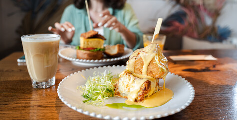 Trendy breakfast in hipster restaurant, cafe. Creative square-shaped croissant in form of cube on skewer. Served with hot cheese in small gravy boat, coffee latte. Citylife meal, meating with friend