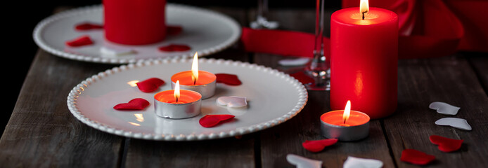 Saint Valentine's Day celebration. Red burning candles, hearts, gift box, postcard on dark wooden background. Happy holiday. Table decor for festive dinner, romantic atmosphere. Banner