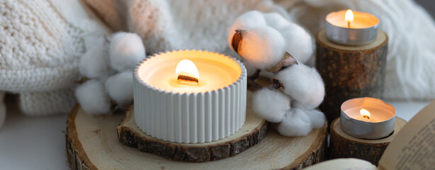 Obraz na płótnie Canvas Cozy autumn or winter composition with aromatic candle, wool sweater, cotton, book. Aromatherapy, home atmosphere of cosiness and relax. Wooden background close up. Banner