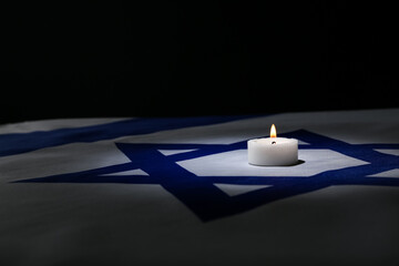Burning candle on flag of Israel against dark background with space for text. International...