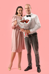 Young couple with bouquet of flowers on pink background. Valentine's Day celebration