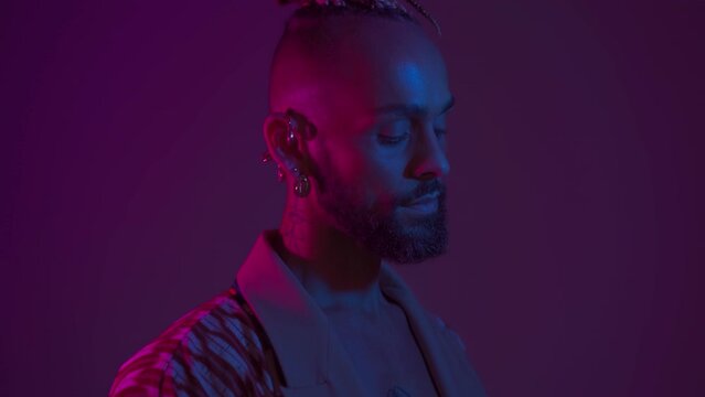 Neon light studio close-up portrait handsome black gay man looking camera. Seductive sexy man wear make up, transgender person in ultraviolet light. LGBT nightclub and nightlife concept Handheld
