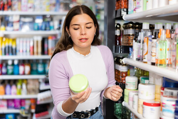 Young woman picking cream from shelf in cosmetics store