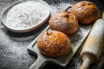 Crusty buns on a cutting Board with flour from the bowl.