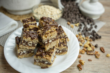 No bake Chocolate oat bars squares served on a white dish surrounded by jars, glass bowl of oats, napkin, chocolate chips,pecans and walnuts. Food. Homemade. bars. Tasty. Delicious. 
squares.