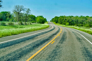 Winding Road in the Texas Countryside, bright green trees grabbing the curve all the way around to the horizon. 
