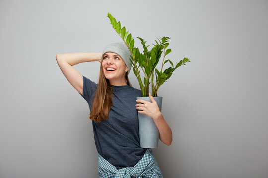 Young woman holding home plant zamioculcas in pot. Portrait of smiling girl looking up.
