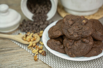 Double chocolate chip cookies freshly baked on a white dish with chocolate chips, walnuts, pecans and wooden spoon.  