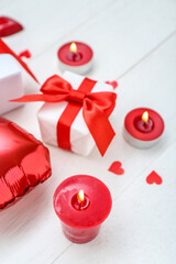 Burning candles and gift boxes on light wooden background. Valentine's Day celebration