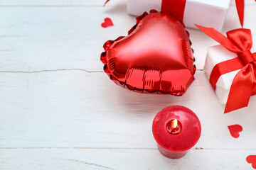 Burning candle, balloon and gift boxes on light wooden background. Valentine's Day celebration