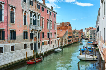 Fototapeta na wymiar Beautiful view of canal in Venice, Italy, with boats on the water surrounded by old picturesque colorful houses under vivid blue sky on spring day.