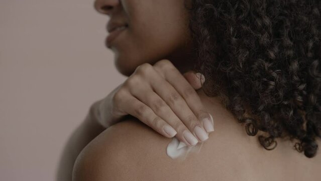 CU Back view, African-American female rubbing cream onto her shoulder. Studio shot, soft lighting. No make up, clean skin. Shot with ARRI Alexa Mini LF