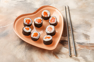 Heart-shaped plate with sushi rolls and chopsticks on grunge background. Valentine's Day celebration