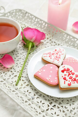Tray with plate of tasty heart shaped cookies, cup of tea and rose flower on table, closeup. Valentine's Day celebration
