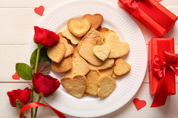 Composition with plate of sweet heart shaped cookies, gifts and rose flowers on light wooden background. Valentines Day celebration