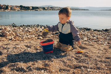portrait of a child collecting stones in a bucket with a shovel on the seashore