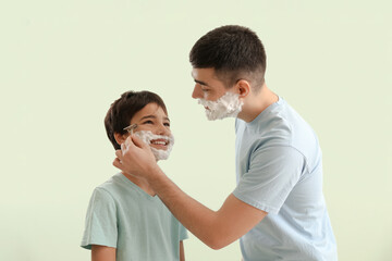 Man and his little son shaving against light color background