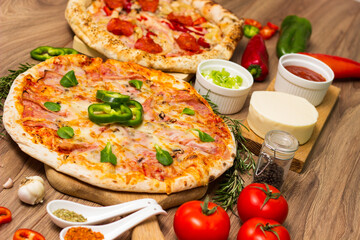 Two different pizza with ingredients on rustic background. Pepperoni pizza and pizza Capricciosa with mozzarella cheese, ham, tomato sauce, salami, mushroom, pepper, spices and fresh basil