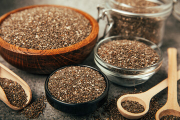 Chia seeds in bowls, spoons and glass jars on a black marble background. SUPERFOOD and antioxidant. Healthy food concept. Gluten free. Copy space.