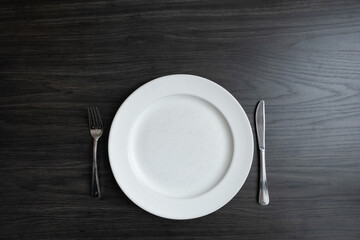 Empty plate with fork and knife on a dark wood table