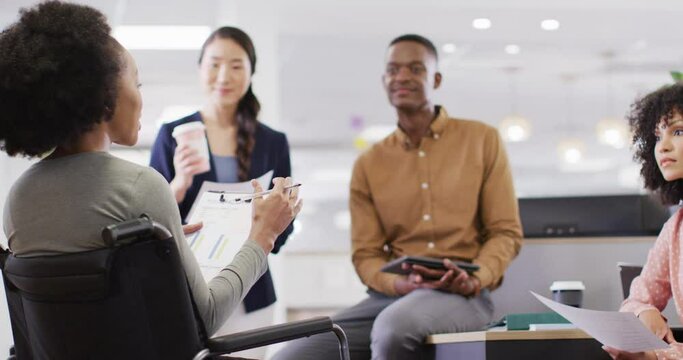 Group of diverse and disabled business people holding documents and talking in office, slow motion