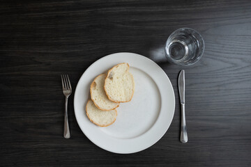 Plate with three slices of white bread and a glass of water on a dark wood table with copy space