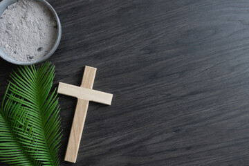 Lent border of palm leaves, cross and bowl of ashes on dark wood with copy space