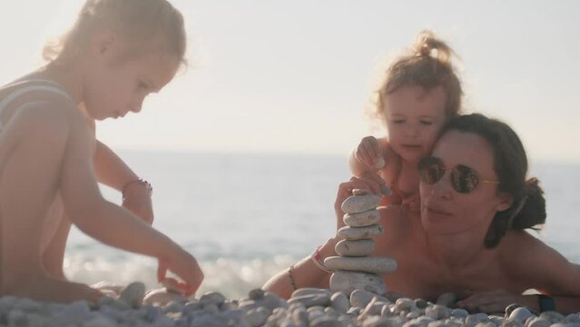 Mom and her two little kids spending time on the beach. Building a pebble tower together, family life balance concept