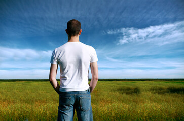 Rear view of young man overlooking farmland in summer.