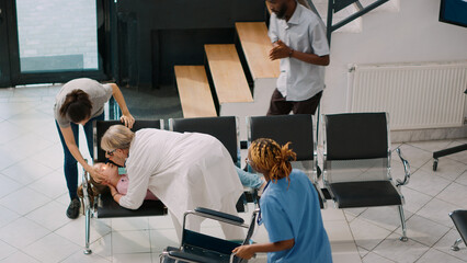 Worried father carrying unconscious child in hospital lobby, kid fainting and parents asking physician for help. Senior medic and nurse consulting young sick girl in health center. Handheld shot.