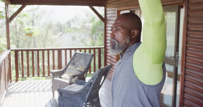 Happy senior african american man spending time in log cabin, doing yoga and stretching, slow motion