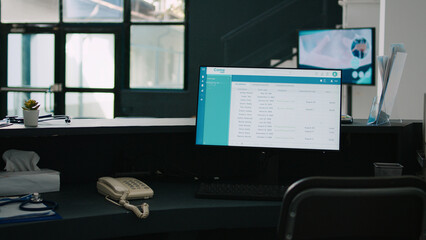 Hospital reception counter with computer showing appointments list, empty waiting room in health center. Medical examinations form on monitor at waiting area front desk, clinical advice.
