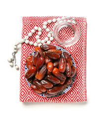 Plate of dates, prayer beads and glass of water for Ramadan on white background
