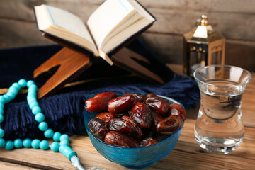 Bowl with dried dates and glass of water for Ramadan on wooden table, closeup