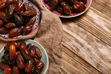 Plates with dried dates and napkin for Ramadan on wooden background