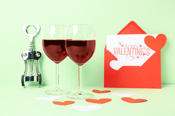 Glasses of wine, envelope with greeting card and opener on green background. Valentine's Day celebration