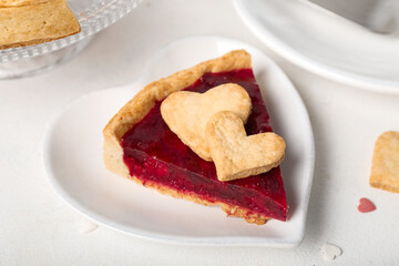 Heart-shaped plate with piece of sweet strawberry pie and cookie hearts for Valentine's day on white table