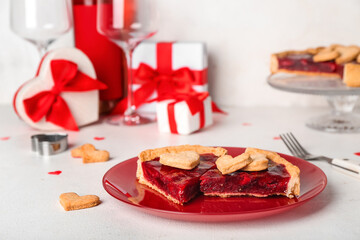 Red plate with pieces of sweet strawberry pie, cookie hearts and gifts for Valentine's day on white table