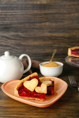 Heart-shaped plate with pieces of sweet strawberry pie and cookie hearts on wooden table
