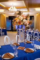 Festive table with blue cloth, napkins, plates, cutlery and glasses prepared for guests in restaurant. Beautiful floral arrangement in gold metal vase with number four. Amazing servings