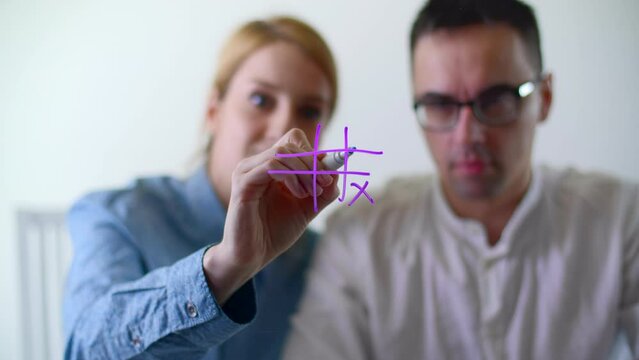 Two players take turns putting Os or Xs in a pattern of nine squares. Coworkers resting while playing game on a glass board. High quality 4k footage