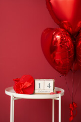 Calendar with date 14 FEBRUARY, candles and gift on table in room