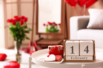 Calendar with date 14 FEBRUARY, cookies and gift on table in living room, closeup