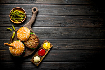 Burgers on a cutting Board with a knife and gherkins in a bowl.