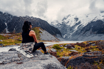 Female hiker Looking Out At Melted Glacial Lake Surrounded By Snow Covered Mountains in Mount Cook National Park, New Zealand