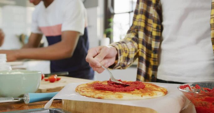 Happy diverse male teenage friends preparing pizza in kitchen, slow motion